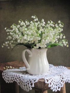 a white vase filled with flowers sitting on top of a wooden table next to a lace doily