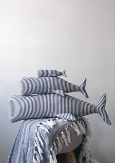 a pile of pillows sitting on top of a wooden stool next to a wall with a white and blue striped pillow