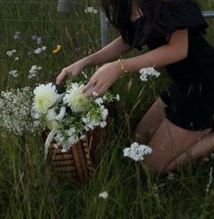 a woman kneeling down next to a basket with flowers in it on the grass near a fence