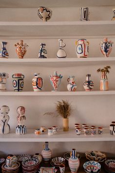 a shelf filled with lots of colorful vases on top of white shelving units