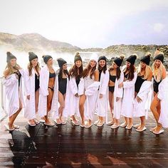 a group of women standing next to each other in bathing suits on a wooden deck