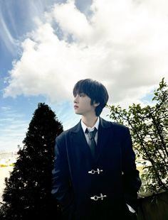 a man wearing a suit and tie standing in front of a blue sky with clouds