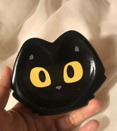 a hand holding a black cat shaped rock with yellow eyes