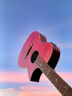 a pink guitar is hanging upside down in front of a blue and white sky with clouds