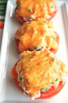 three stuffed tomatoes on a white plate with green onions and carrots in the background