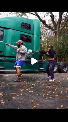 two men are dancing in front of a green truck with trees and leaves on the ground