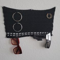 a pair of glasses and some rings hanging on the wall next to a knitted piece of cloth