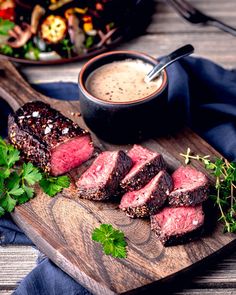 steak on a cutting board next to a bowl of sauce