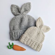 two knitted hats and a carrot on a white surface, one has a bunny ear