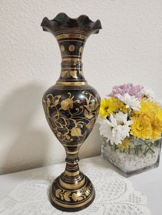 a vase sitting on top of a white table next to a flower pot filled with yellow and purple flowers