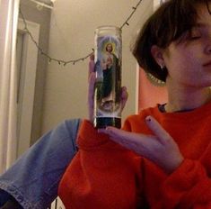 a woman in an orange sweater holding up a cell phone with the image of jesus on it