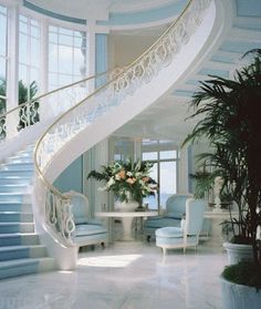 a spiral staircase in the middle of a room with blue chairs and potted plants