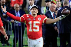 a man holding a football in his right hand and wearing a red jersey with the number 15 on it