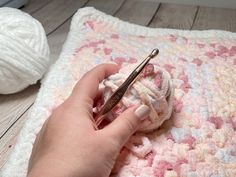 someone is crocheting on a blanket with yarn and a pair of scissors in their hand