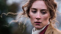 a woman with freckled hair is looking at the camera while wearing a brown coat