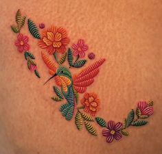 an embroidered hummingbird on the back of a woman's shoulder with flowers and leaves