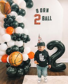 a young boy wearing a birthday hat standing in front of some balloons and basketballs