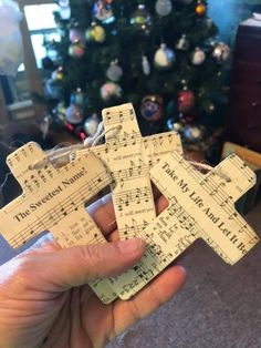 someone holding up some sheet music crosses in front of a christmas tree