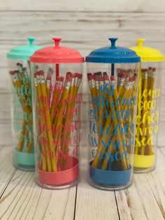 three colored pencils are in a glass container on a wooden table next to each other