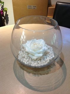 a glass bowl with pearls and a white rose in it on top of a table