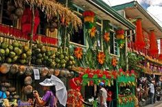 many people are walking down the street in front of some colorful buildings and fruit stands