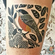 a bird sitting on top of a tree branch next to leaves and flowers in front of a woman's leg