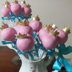 there are pink cake pops with gold crowns on them in a white vase filled with blue ribbon