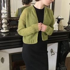 a woman standing in front of a mirror wearing a green cardigan sweater and black dress