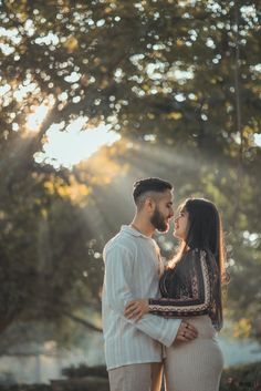 a man and woman standing next to each other in front of trees with the sun shining down on them