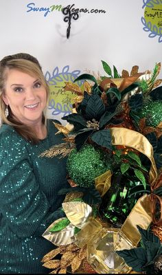 a woman standing next to a green and gold christmas tree in front of a wall