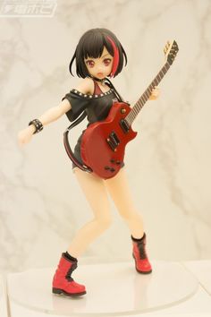 a doll is holding a red guitar and posing for the camera while standing on a white surface