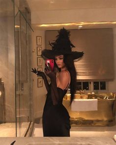 a woman is taking a selfie in the bathroom with her cell phone while wearing a black dress and hat