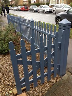 a blue picket fence sitting next to a sidewalk with cars parked on the street behind it