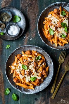 two bowls filled with pasta and meat on top of a wooden table next to silverware