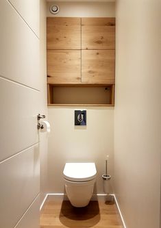 a white toilet sitting inside of a bathroom next to a wooden cabinet above the toilet