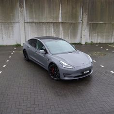 a grey tesla car parked in front of a white wall with black rims and red brake pads