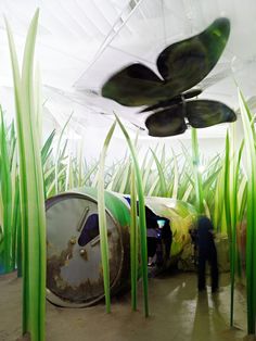 a man standing in the middle of a room with green plants growing out of it