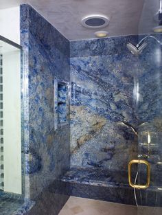 a bathroom with blue marble walls and flooring, shower head in the corner next to glass doors