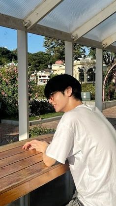 a young man sitting at a wooden bench on top of a porch next to a building