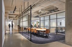 an office with glass partitions and tables in the center, along with people walking by