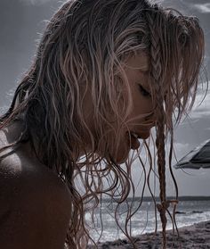 a woman standing on top of a sandy beach next to the ocean with long hair