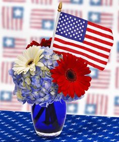 an american flag in a blue vase with red, white and blue flowers on a table