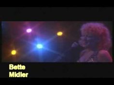 a woman singing into a microphone in front of colorful lights and the words bette midler