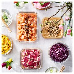 several different types of food in plastic containers on a white table with flowers and chopsticks