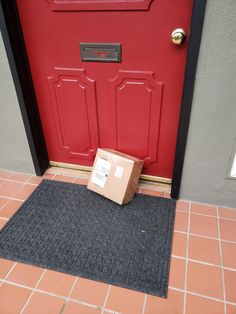 a cardboard box sitting on the floor in front of a red door with a black mat