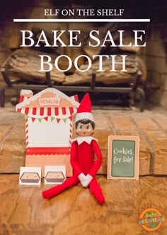 an elf is sitting on the floor next to a fake house and sign that says bake sale booth