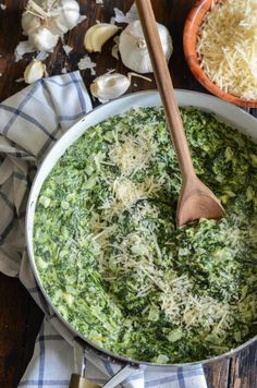 a pot filled with spinach and parmesan cheese on top of a wooden table