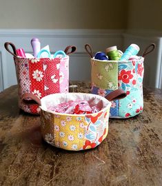 three colorful storage baskets sitting on top of a wooden table next to yarn and scissors