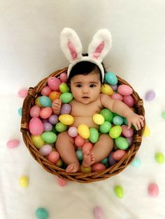 a baby sitting in a basket filled with eggs and bunny ears on top of it