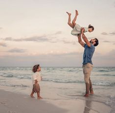 a man holding a child up in the air while standing on top of a beach